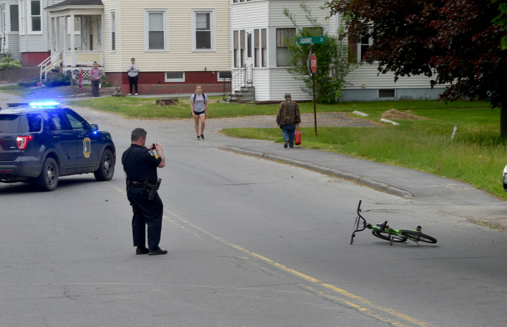 A Waterville police officer takes photos of the scene where a child struck a car while riding his bicycle Tuesday on Western Avenue in Waterville.