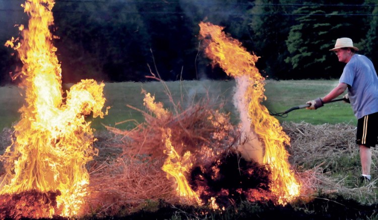 Peter Clifford throws a pitchfork full of burning brush to ignite another pile while he and his father Roger burned a field in Benton on Monday August 25, 2014.