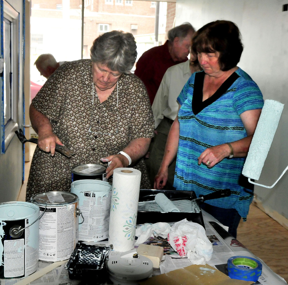 REM Co-executive Director Faye Nicholson, left, opens cans of paint for volunteers painting the new REM offices Tuesday on Temple Street in Waterville.