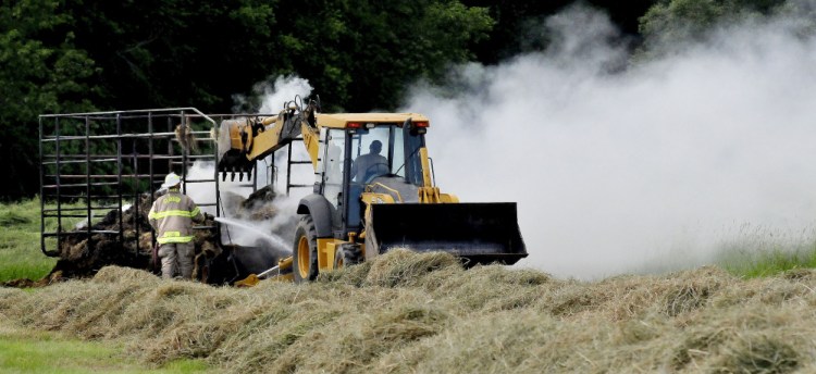 As a Clinton firefighter spays water on smoldering hay a bucket loader operator prepares to knock the hay off a wagon that was destroyed by fire in a field off Gogan Road in Clinton on Sunday.