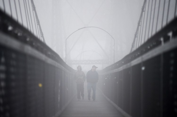 Two people walk across the Two Cent Bridge on March 1 over the Kennebec River as a thick fog settles on Waterville.
