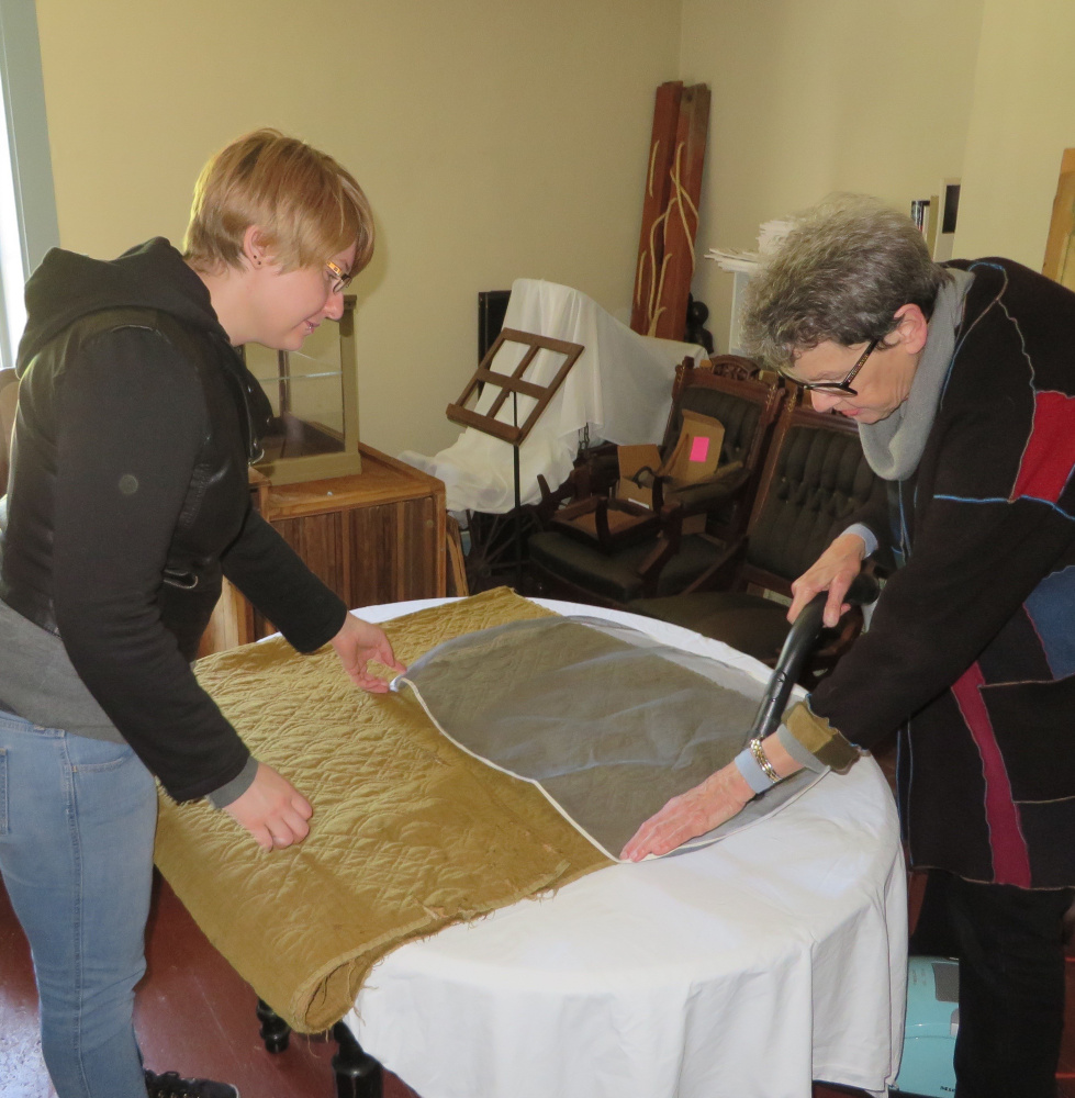 Katie Likens, left, a graduate student at the University of Rhode Island, and JoAnn Stabb, professor emerita, University of California at Davis, use a special vacuum to clean one of Lincoln County Historical Association's 18th century quilts with a special vacuum. The soft mesh screen prevents fibers from breaking.
