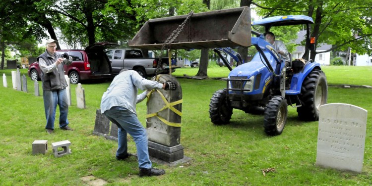 The headstone of Samuel and Sally Jewett is re-erected Tuesday at their grave in the churchyard at the former site of St. Anne's Church in Gardiner. Taking photos at left is Bill King as Hank McIntyre sets the stone while Logan Johnston lowers it from his tractor.
