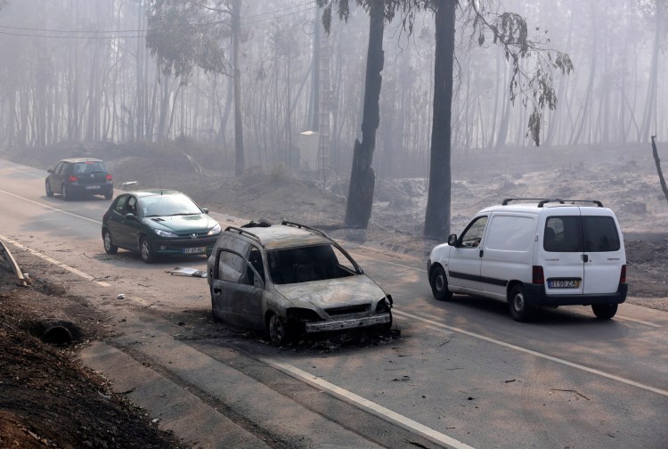 Cars drive past a burnt vehicle on the road between Castanheira de Pera and Figueiro dos Vinhos, central Portugal, on Sunday.