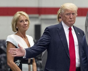 FILE - In this June 13, 2017, file photo, President Donald Trump, accompanied by Education Secretary Betsy DeVos, left, waves to members of the media as he takes a tour of Waukesha County Technical College in Pewaukee, Wis. Democratic attorneys general in 18 states and the District of Columbia are suing Education Secretary Betsy DeVos over her decision to suspend rules meant to protect students from abuses by for-profit colleges. The lawsuit was filed Thursday, July 6, 2017,  in federal court in Washington and demands implementation of borrower defense to repayment rules. (AP Photo/Andrew Harnik, File)