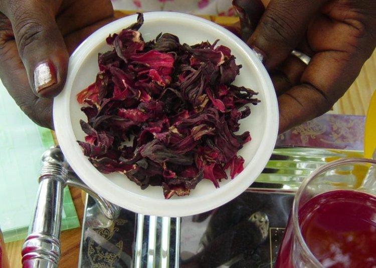 A woman holds
karkaday, hibiscus petal tea, next to a glass of it prepared and presented on a silver tray. In Sudan the tea is often cold-brewed, then strained, and served as a cool drink to counter the heat.