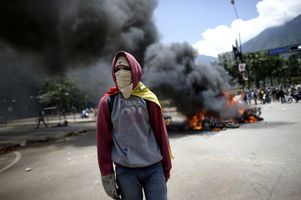 A demonstrator walks near a pile of burning motorcycles during clashes between police and anti-government protesters in Caracas, Venezuela, on Sunday. After an explosion injured several officers, police were seen throwing privately owned motorcycles into the fire.