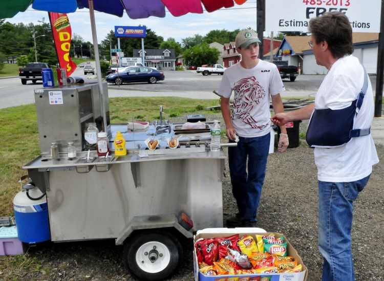 Dana Purington, left, owner of Dana's Dogz food stand, takes money from customer Jeff Greenlaw at his mobile hot dog stand parked off Maine Avenue in Farmingdale on Monday.