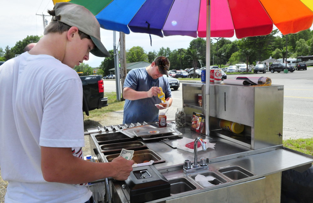Dana Purington, left, owner of Dana's Dogz food stand, takes money from customer John Michaud who is putting mustard on a hot dog at his mobile hot dog stand parked off Maine Avenue in Farmingdale on Monday.