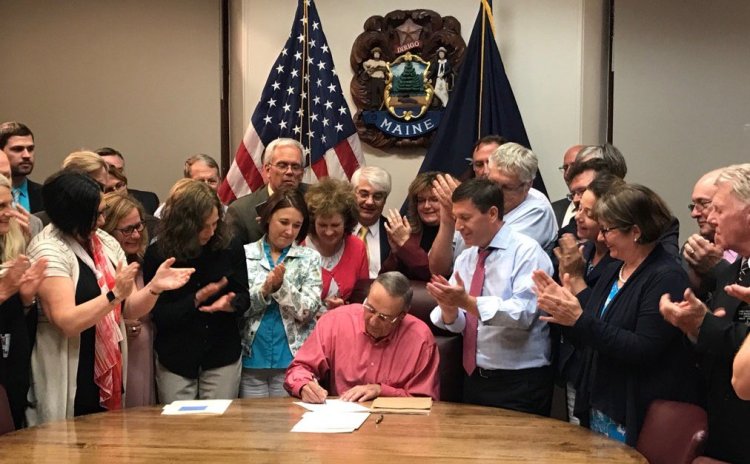 Gov. Paul LePage signs the state budget early Tuesday morning as Republican lawmakers applaud.