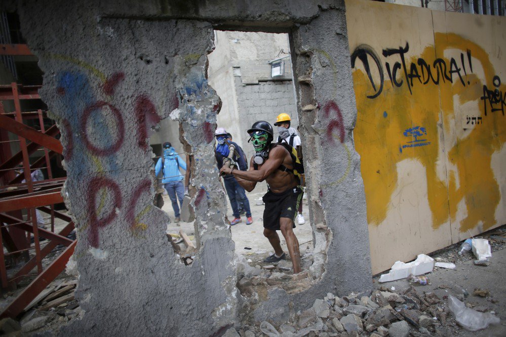 An anti-government demonstrator whacks a wall to release pieces of concrete to throw at Venezuelan Bolivarian National Police.
