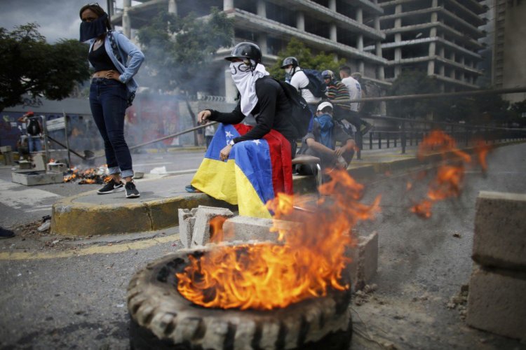 Masked anti-government demonstrators stand next to a burning barricade during a protest against the installation of a constitutional assembly in Caracas, Venezuela.