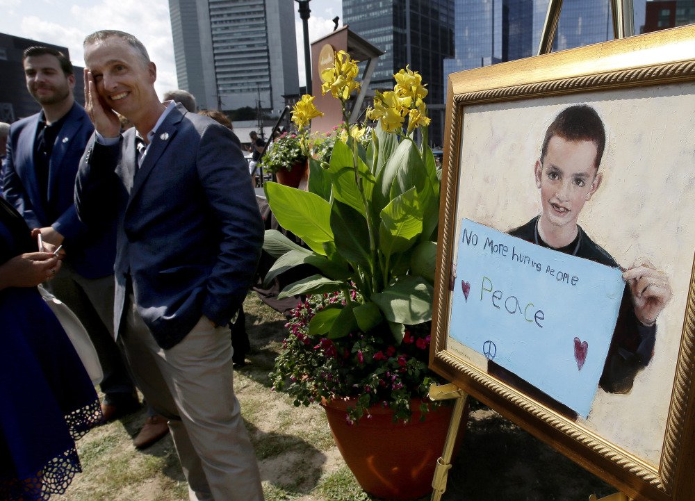 Bill Richard, second from left, father of fatal Boston Marathon bombing victim Martin Richard, brings his hand to his face while standing next to a painting of Martin, right, at the conclusion of groundbreaking ceremonies for a park named after his late son, Wednesday, Aug. 16, 2017, in Boston. Martin Richard, 8, was the youngest of three people killed when two bombs exploded near the Boston Marathon finish line on April 15, 2013. (AP Photo/Steven Senne)