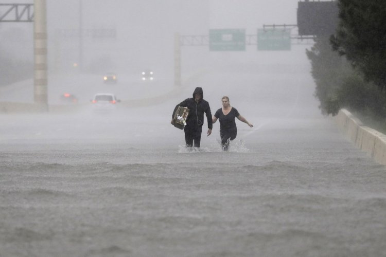 Two people walk down a flooded section of Interstate 610. 
