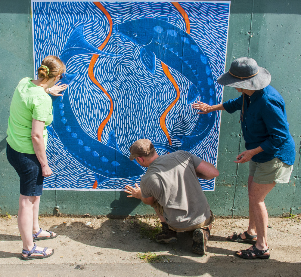 From left, Barbara Whitten, Kerstin Gilg and Christine Olsen smooth out air bubbles after hanging a large-scale print Saturday on the bottom of Dennis' Pizza in the Arcade parking lot in Gardiner. The 6-by-6 foot print is of a 12-by-12-inch reduction linocut titled "Endangered Shortnose Sturgeon," done by Olsen. It was the first of several new large-scale paper prints to be attached to several walls with wheat paste that day. The event was a preview of the next Artwalk Gardiner, which is scheduled for 5:30 to 8 p.m. Friday in downtown Gardiner.