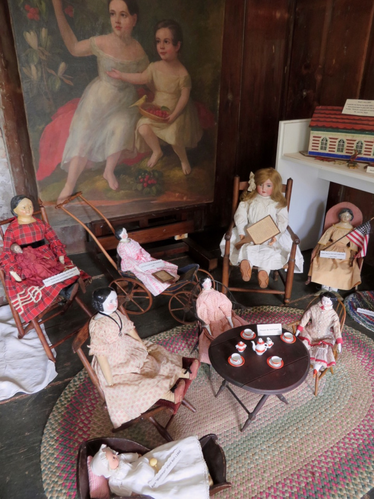 A selection of dolls arranged before a painting of children who lived at the Pownalborough Court House in the mid 1800s were common over the course of nearly 100 years. The dolls and other toys will be on exhibit until Columbus Day.