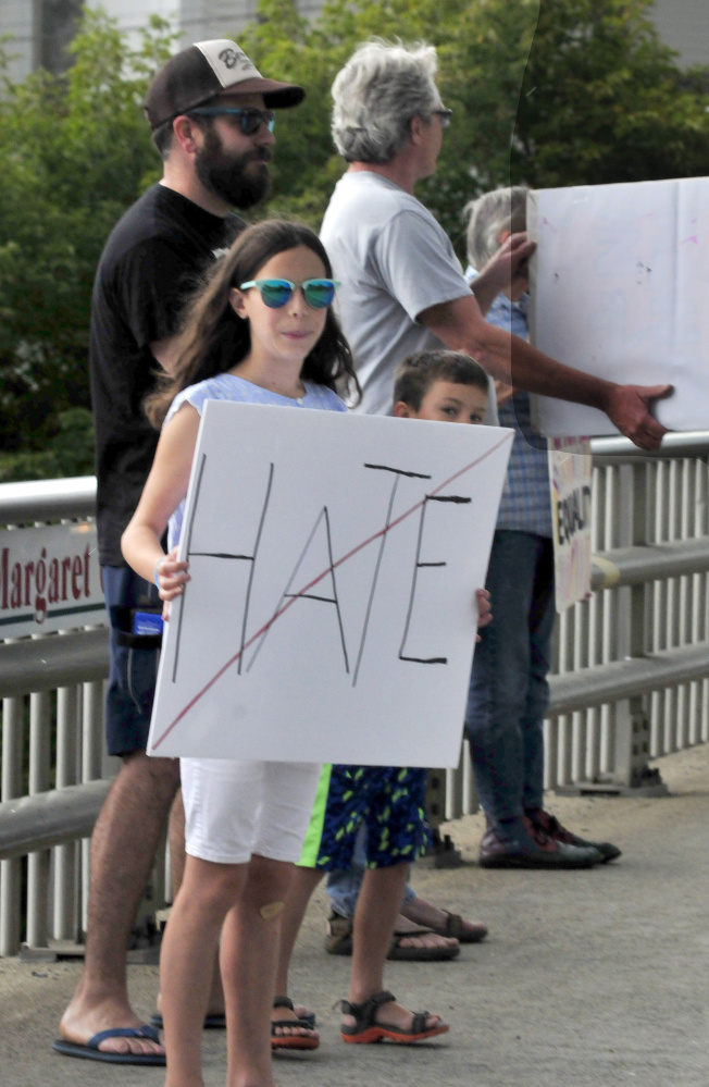 Carly and Finn McCabe and their father, Jeff, hold signs among protesters with Stand With Charlottesville Against White Supremacy in Skowhegan on Sunday.