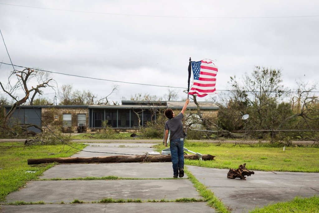Layton Carpenter walks down a debris-littered driveway in Bayside, Texas, on Sunday holding a broken American flag that he found in the water after Hurricane Harvey hit.