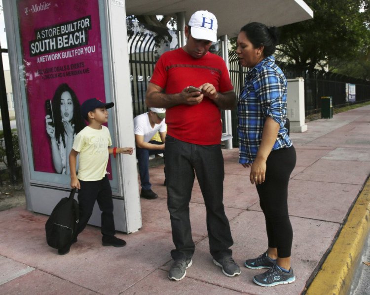 Wilman Hernandez and his wife, Brenda Ramirez, check their phones for the location of shelters and their capacity while waiting for a bus in Miami Beach, Fla. Meanwhile, the main hub leading Floridians out of Hurricane Irma's path is bumper to bumper with those who can afford to escape.
