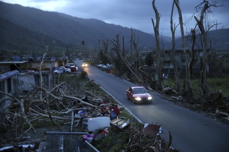 In this Sept. 26 photo, neighbors sit on a couch outside their destroyed homes as sun sets in the aftermath of Hurricane Maria, in Yabucoa, Puerto Rico. A Maine woman who has family on the island has organized a restaurant fundraiser to provide relief to island inhabitants.