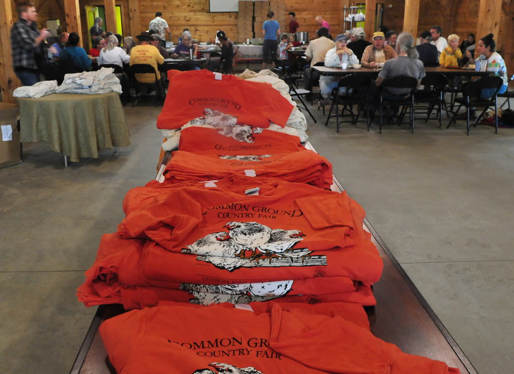 Some of the 2,850 volunteers have lunch near piles of T-shirts for the Maine Organic Farmers and Gardeners Association 41st annual Common Ground Country Fair in Unity on Monday. The fair runs this Friday through September 24.