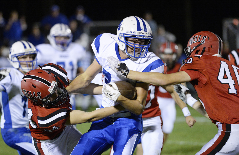 Madison ball carrier Jacob Meader is tackled by Wells defenders Peyton MacKay, left, and Ethan Marsh of Wells during a Class D South game Friday night.