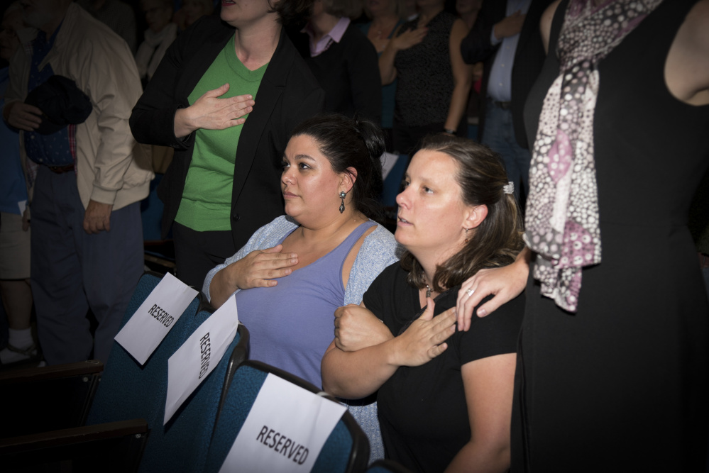 April Fournier, left, of Portland, and Liz Smith, of Camden, kneel while reciting the Pledge of Allegiance during the opening of a Democratic gubernatorial candidates' forum held Thursday evening at the University of Maine at Augusta. Zak Ringelstein led the Pledge of Allegiance and invited attendees to stand or kneel.