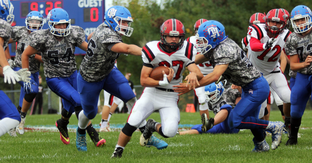 Wells High School's Chad Fitzpatrick runs past Oak Hill High School's Bailey Drouin, left, and Cruz Poirier, right, during a first-half carry in Wales on Saturday.