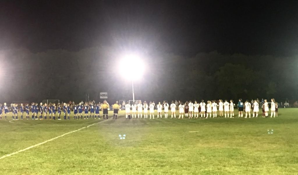 The Madison and Monmouth girls soccer teams line the field under the lights during introductions prior to their match Saturday night in Monmouth.