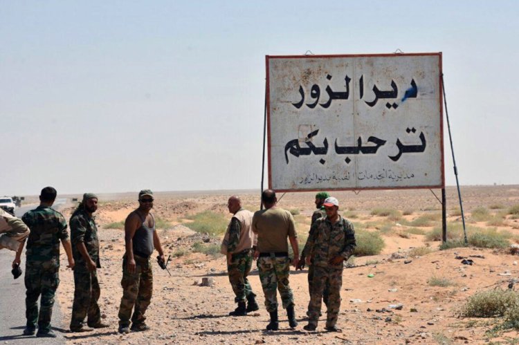 A Sept. 3 photo shows Syrian troops and pro-government gunmen standing next to a placard in Arabic which reads "Deir el-Zour welcomes you" in the eastern city of Deir el-Zour, Syria. The oil-rich eastern Deir el-Zour province straddles the border with Iraq.