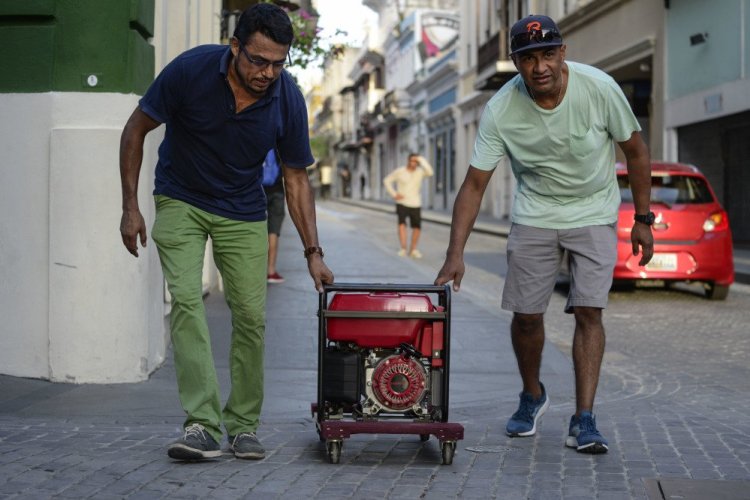 Residents push a generator along the street in San Juan, Puerto Rico, on Friday. In the month since Hurricane Maria, a third of the hotels remain shuttered and many shops and restaurants are closed.
