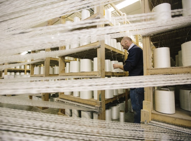 Kirk Hall checks on the fiberglass “yarn packages” feeding into an industrial loom making heat-resistant fabric at Auburn Manufacturing in Mechanic Falls.
