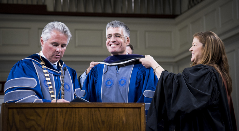 Colby College Marshal Annie Kloppenberg, right, assists in placing an honorary degree hood on Lovejoy Award Recipient Alec MacGillis, center, at Convocation ceremonies on Monday night at Lorimer Chapel on the college campus as Colby College President David Greene, left, reads the citation.