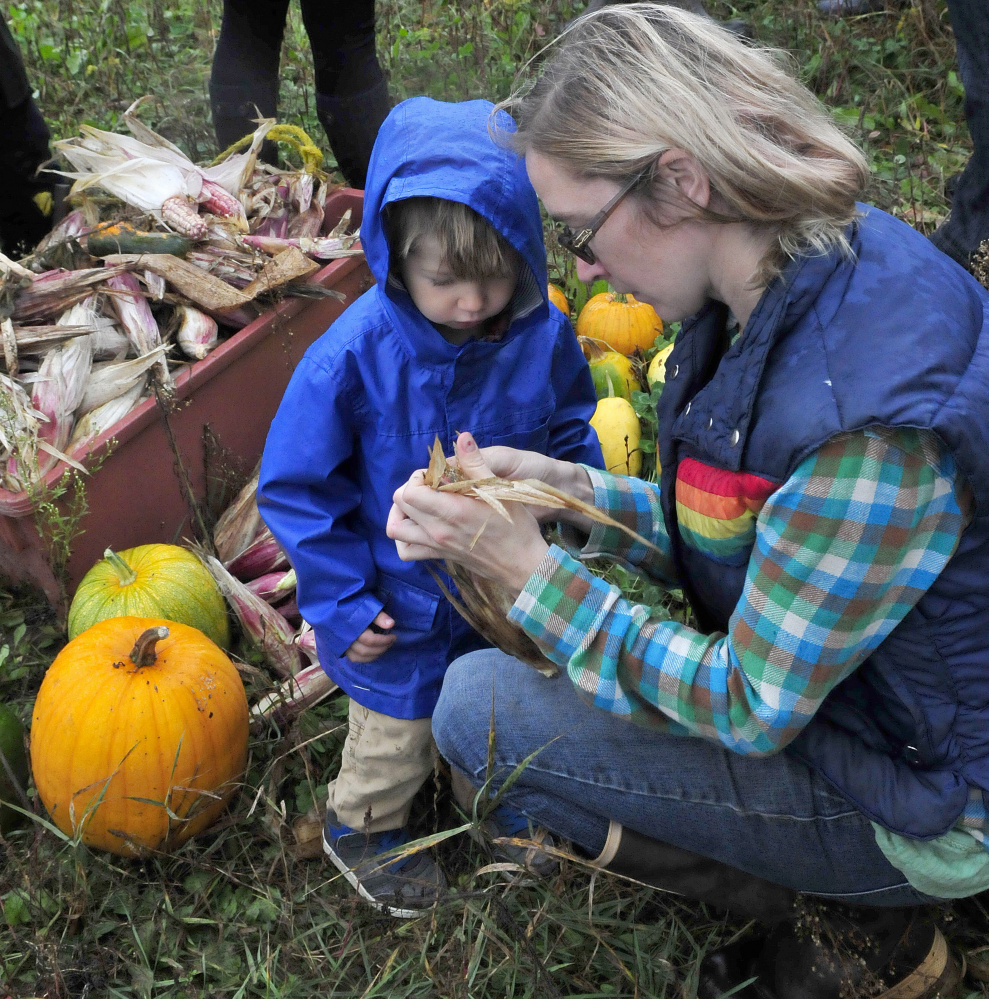 Cate Jacques shows her son Theodore corn produced using the Three Sisters planting technique of planting corn, squash and beans in a single mound during an Indigenous Peoples Day celebration at the Sweet Land farm in Starks on Monday.