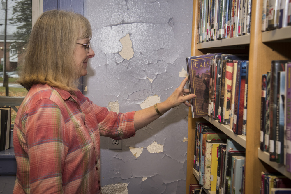 Lynn Howker, Monmouth Middle School librarian, returns a book to the shelf Wednesday next to a library wall with chipped and cracked paint. The library is housed in a century-old building.