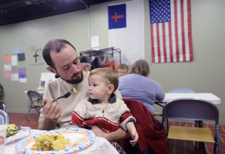 Brad Smith of Steep Falls, a village in Standish, offers his year-old son, Jensen, a bite of food during dinner Thursday at The Deeper Well Church in Standish. The church has provided the blackout-stricken community a warm refuge and hot meals every night since Monday's storm.