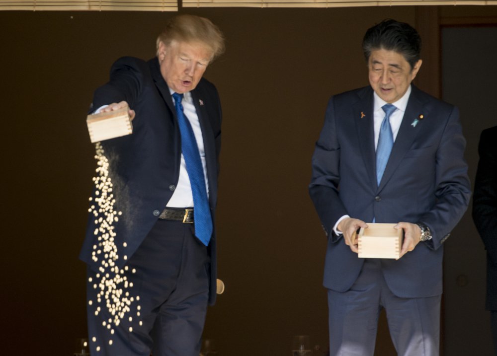 President Trump pours out the remainder of his fish food as he and Japanese Prime Minister Shinzo Abe feed fish in a koi pond at the Akasaka Palace in Tokyo on Monday. Trump is also traveling to South Korea, China, Vietnam and the Philippines.