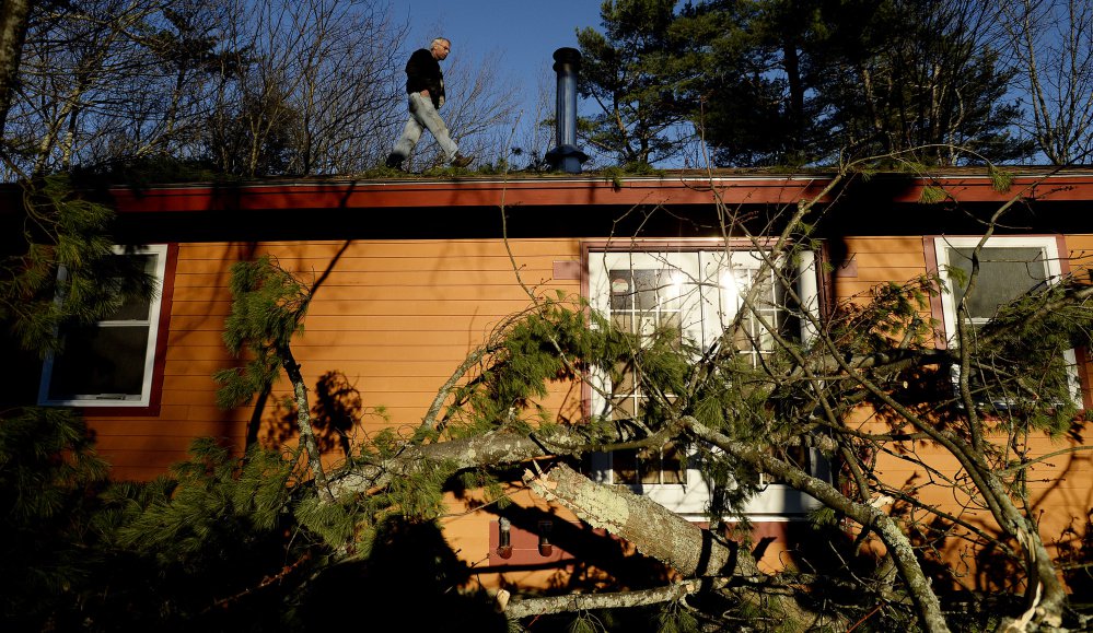 Ron Bozzuto inspects the roof of his Westbrook home after high winds knocked down a tree Friday. The tree landed just in front of his home but did bring down the power lines.