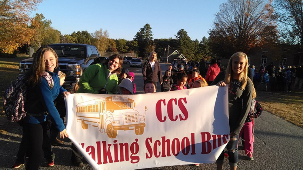 Charlee Davis, left, and Breanna Rainville, right, hold Carrabec Community School's sign prior to its October Walking School Bus event.