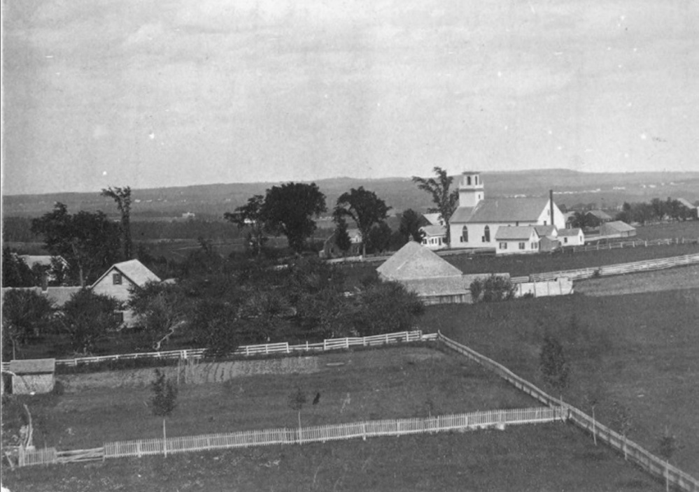 From the tower atop Bearce Hall at Kents Hill School before 1872, looking east over Kents Hill Village. Torsey Methodist Church can be seen in the foreground and in the distance is Readfield Depot.