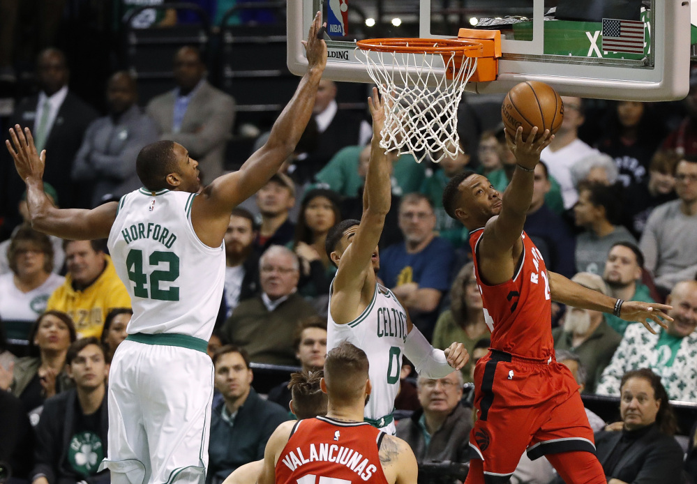 Toronto Raptors' Norman Powell, right, goes under the basket to shoot past Boston Celtics forwards Jayson Tatum and Al Horford (42) during the first quarter Sunday at TD Garden in Boston.