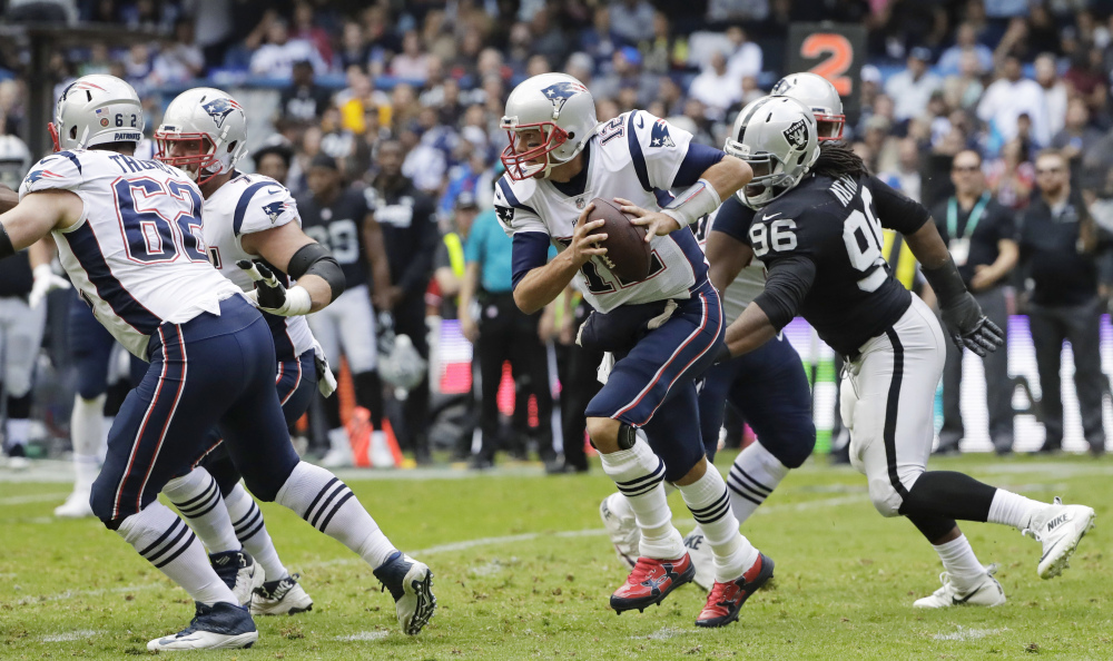 New England Patriots quarterback Tom Brady, center, scrambles against the Oakland Raiders during the first half Sunday in Mexico City.