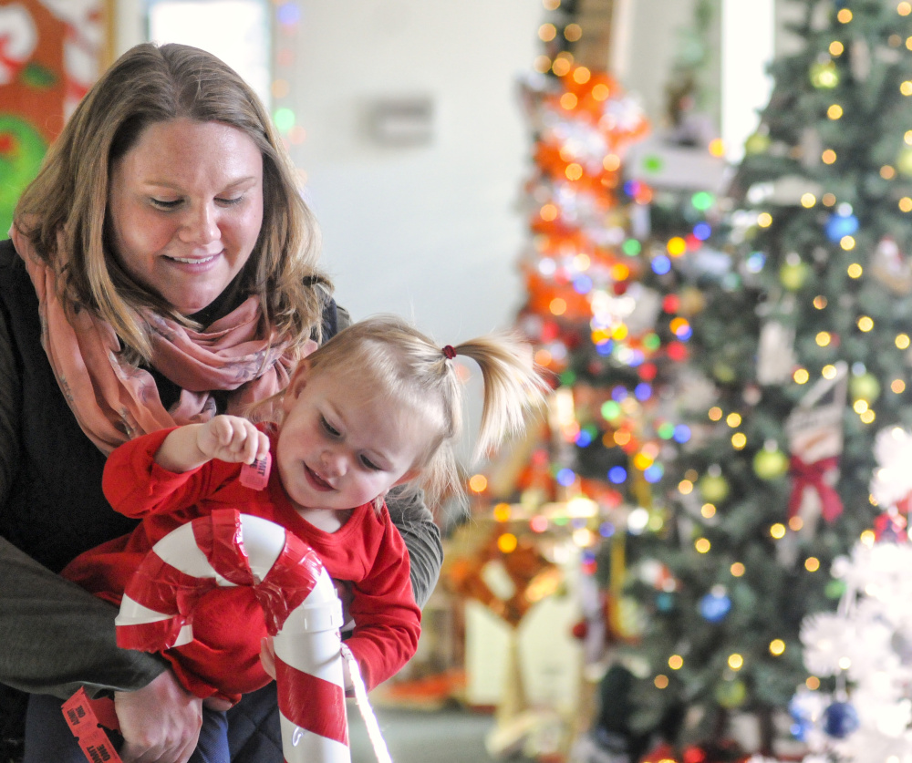 Marie Woodcock, left, holds her daughter Emma McKenna as she drops a ticket into a PVC pipe candy cane to vote for one of her favorite trees Friday at the River of Trees event in downtown Augusta.