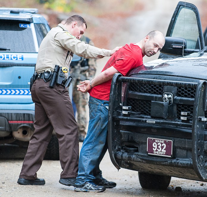 An Oxford County Sheriff's deputy pats down Jason Merriam on Bradeen Road in Sumner on Friday morning after he was brought out of the woods where Maine State Police Tactical Team members took him into custody.