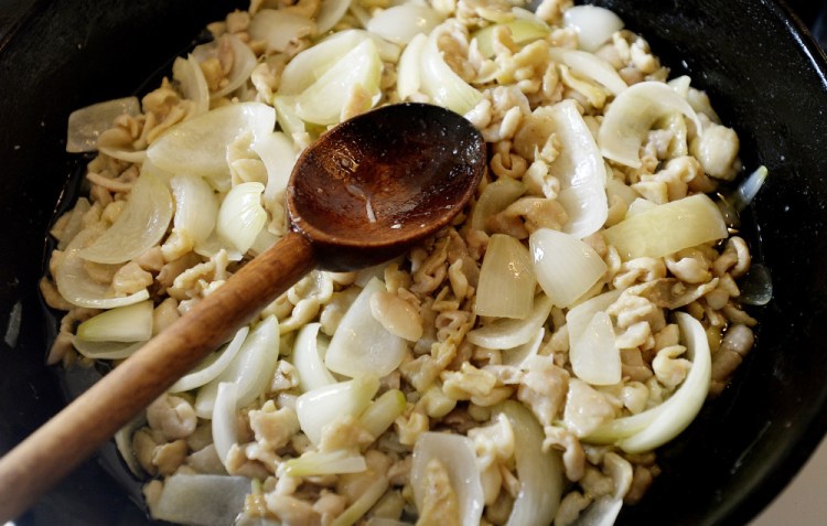 Bits of chicken skin and onion cook slowly in a cast-iron pan. 