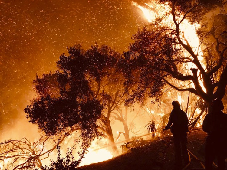 In this photo released Sunday by the Santa Barbara County Fire Department, firefighters knock down flames as they advance on homes atop Shepherd Mesa Road in Carpinteria, California. A flare-up on the western edge of Southern California's largest and most destructive wildfire sent residents fleeing.