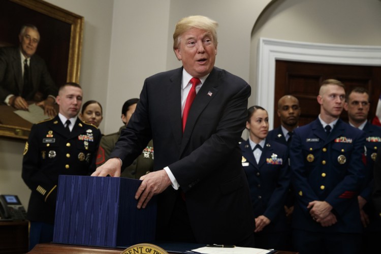 President Trump holds onto a box containing the National Defense Authorization Act in the Roosevelt Room of the White House on Tuesday.
