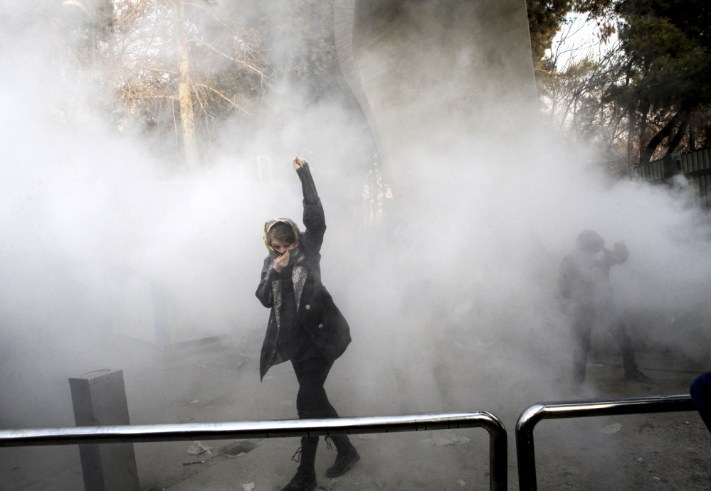 A university student attends a protest inside Tehran University while a smoke grenade is thrown by anti-riot police in Tehran, Iran, on Saturday. A wave of spontaneous protests over Iran's weak economy swept Tehran on Saturday, with college students and others chanting against the government just hours after hard-liners held their own rally.