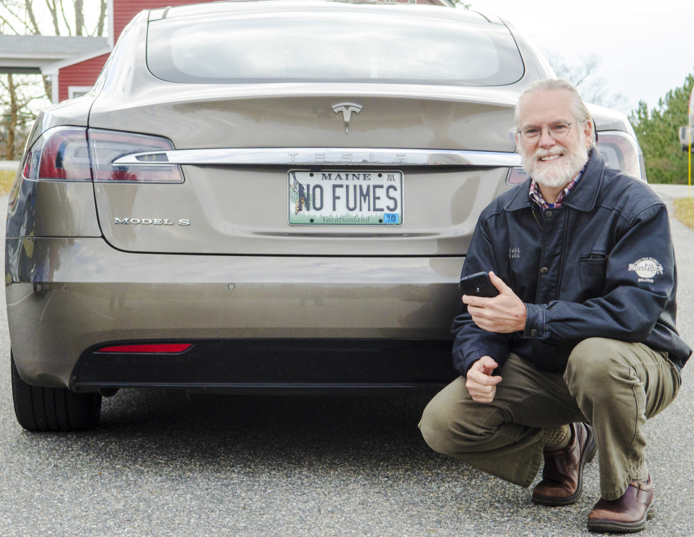 Scott Cowger holds up his phone with the Uber app on it on Wednesday beside his Tesla in Hallowell.