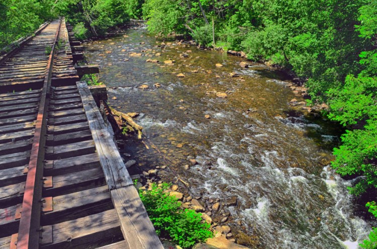 Cobbossee Stream in Gardiner is seen in June 2016 flowing under a railroad trestle. Officials are nearing completion of a plan for building a trail along the stream and are seeking input from downtown business owners on the impact of some design decisions.